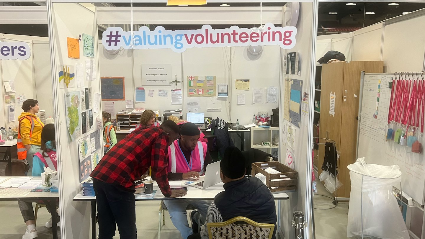 Volunteers stand at an exhibition booth discussing work on a laptop.