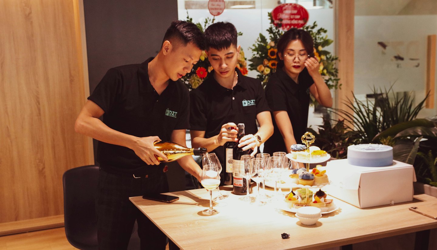Three colleagues preparing drinks and desserts for a corporate celebration.